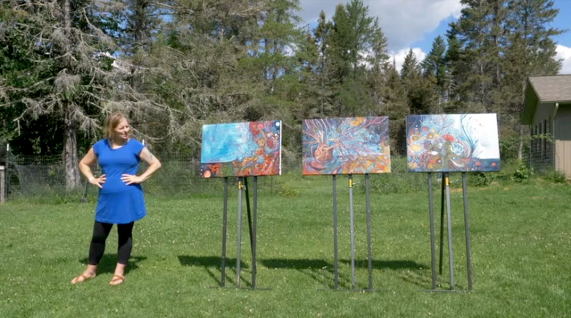 photo of sarah brokke standing next to three canvases on easels in her yard