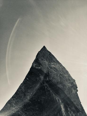 black and white Photograph of a triangular rock formation against the sky with light reflections arcing around it
